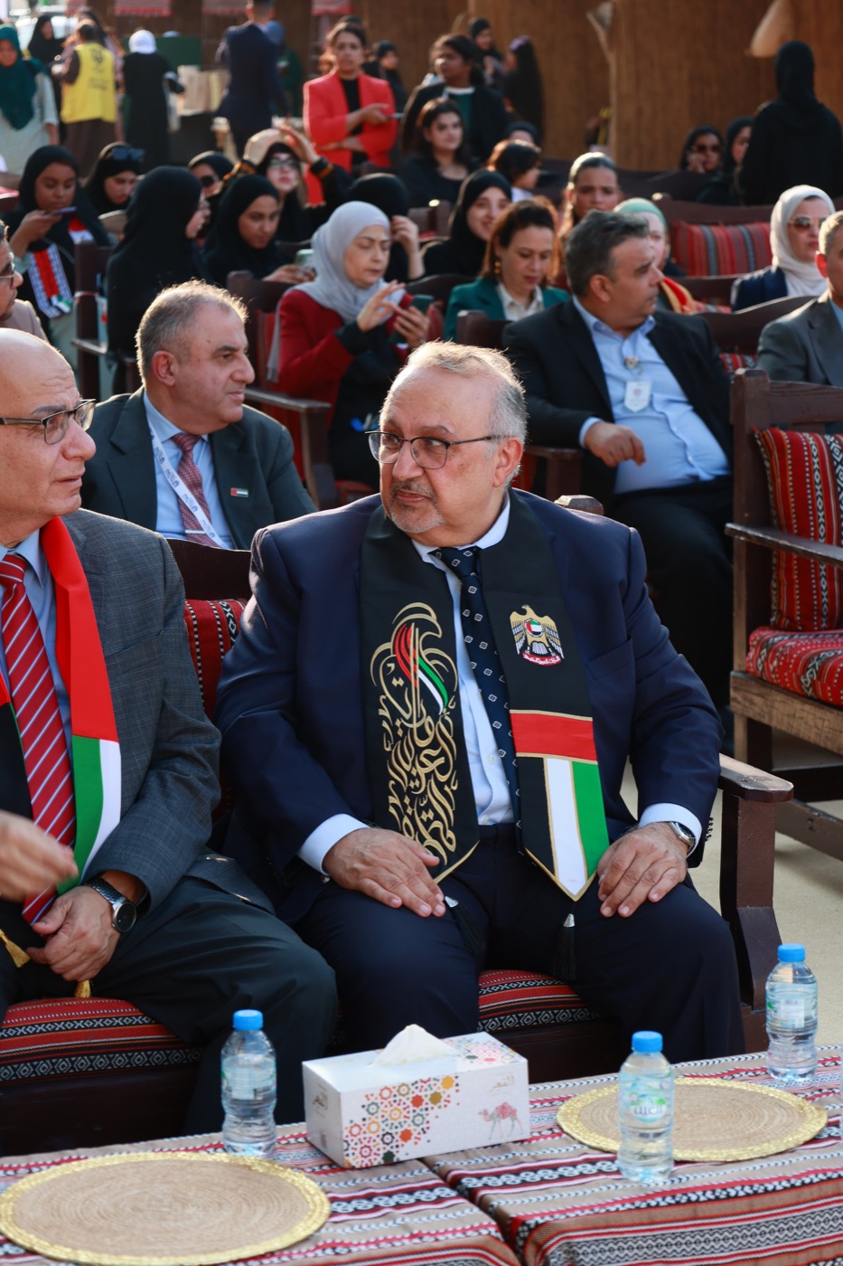 Professor Badran A. Badran seated at an outdoor UAE celebration, wearing a sash in the colors of the UAE flag